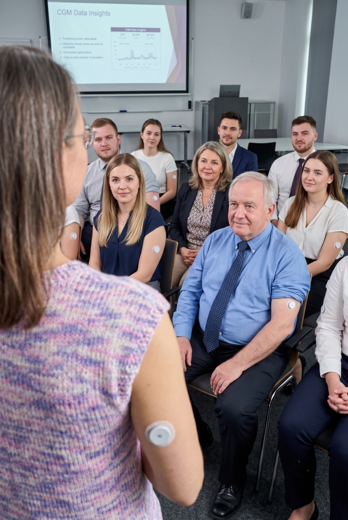 A professional giving a presentation about CGM data insights to a team of employees wearing continuous glucose monitors.